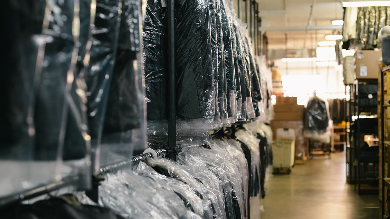 Una lunga fila di capi puliti appesi nelle custodie di plastica, nel retro di una tintoria